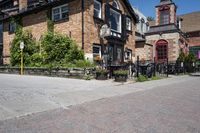 a brick building sitting next to a sidewalk with lots of chairs and umbrellas hanging from it and a car parked outside