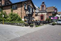 a brick building sitting next to a sidewalk with lots of chairs and umbrellas hanging from it and a car parked outside