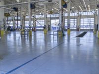 some people in an indoor building with blue lines on the floor and yellow poles at the entrance