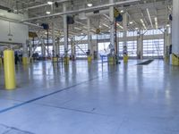 some people in an indoor building with blue lines on the floor and yellow poles at the entrance