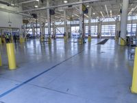some people in an indoor building with blue lines on the floor and yellow poles at the entrance