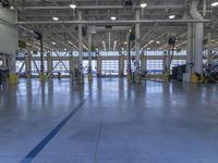some people in an indoor building with blue lines on the floor and yellow poles at the entrance