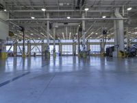 some people in an indoor building with blue lines on the floor and yellow poles at the entrance