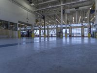 some people in an indoor building with blue lines on the floor and yellow poles at the entrance