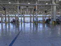 some people in an indoor building with blue lines on the floor and yellow poles at the entrance