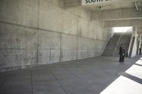 man with a suitcase walking in a hallway on some stairs next to concrete wall and stairs
