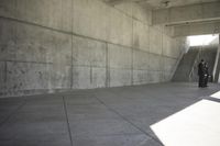 man with a suitcase walking in a hallway on some stairs next to concrete wall and stairs