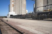 several trains traveling along tracks near tall grain silos in the background, and a blue sky