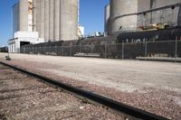 several trains traveling along tracks near tall grain silos in the background, and a blue sky