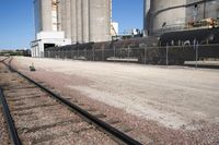 several trains traveling along tracks near tall grain silos in the background, and a blue sky