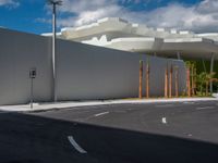 a car drives past an industrial looking white building with palm trees in the foreground