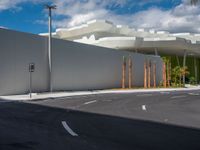 a car drives past an industrial looking white building with palm trees in the foreground