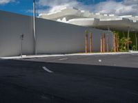 a car drives past an industrial looking white building with palm trees in the foreground