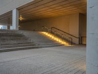 the stairs are lined with concrete steps leading from one room to another that has lights on