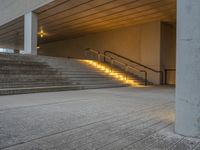 the stairs are lined with concrete steps leading from one room to another that has lights on