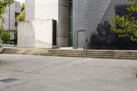 a grey building with three steps going up it next to some green trees and plants