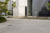 a grey building with three steps going up it next to some green trees and plants