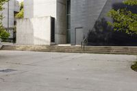 a grey building with three steps going up it next to some green trees and plants