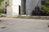 a grey building with three steps going up it next to some green trees and plants