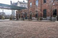 a brick road in front of a red brick building and gate in the background, there is a street sign that says adams and worth on it