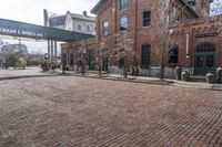 a brick road in front of a red brick building and gate in the background, there is a street sign that says adams and worth on it