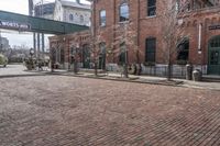 a brick road in front of a red brick building and gate in the background, there is a street sign that says adams and worth on it