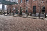 a brick road in front of a red brick building and gate in the background, there is a street sign that says adams and worth on it