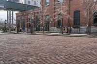 a brick road in front of a red brick building and gate in the background, there is a street sign that says adams and worth on it