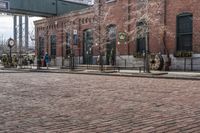 a brick road in front of a red brick building and gate in the background, there is a street sign that says adams and worth on it