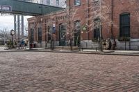 a brick road in front of a red brick building and gate in the background, there is a street sign that says adams and worth on it