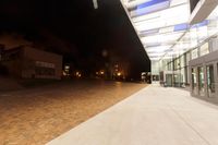 night time photograph showing light on outdoor building's outside entrance and brick walkway through glass windows