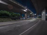 an empty street with a bridge in the background at nighttime in a city near the freeway