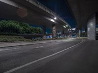 an empty street with a bridge in the background at nighttime in a city near the freeway