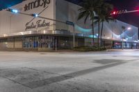 an empty city street at night with an advertising store in the middle and palm trees lining the street