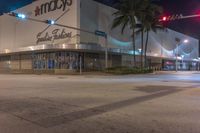 an empty city street at night with an advertising store in the middle and palm trees lining the street