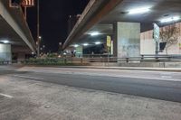 an elevated freeway bridge in night time with a person walking by it and the light from the street lamps shine on