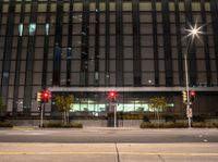 a couple of traffic lights in front of a large building at night with no people on them