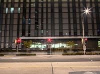 a couple of traffic lights in front of a large building at night with no people on them