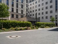 a paved walkway with a white bench on each side of it, and several apartment buildings in the background