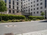 a paved walkway with a white bench on each side of it, and several apartment buildings in the background