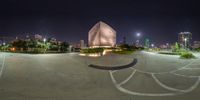 a wide angle of a circular concrete courtyard with lights and trees around it, surrounded by other buildings