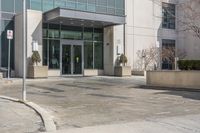 this is a large building with some glass doors on it's doors are open, a street sign on the sidewalk has an empty space in front of the entrance