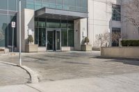 this is a large building with some glass doors on it's doors are open, a street sign on the sidewalk has an empty space in front of the entrance