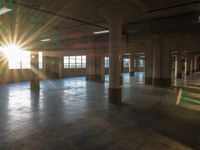 the light is shining into an empty building with columns and concrete floors, it is very bright with just a few bright spots