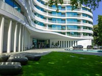 a large white building in front of a swimming pool and a grass lawn area in front