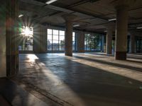 sunlight shining down from behind the windows of an empty building with a concrete floor and exposed ceiling