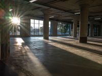 sunlight shining down from behind the windows of an empty building with a concrete floor and exposed ceiling