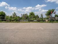 an empty parking lot with benches and trees on the other side of it with a sky background