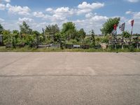 an empty parking lot with benches and trees on the other side of it with a sky background