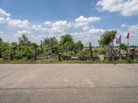 an empty parking lot with benches and trees on the other side of it with a sky background